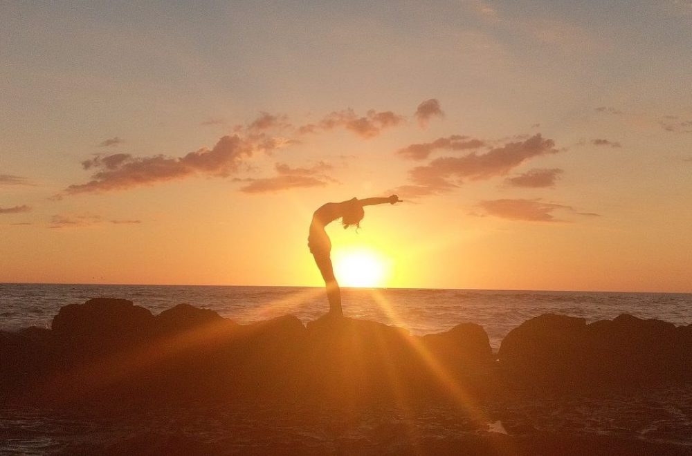 Yoga student performing standing backbend on rocks in front of setting sun at Mexico Yoga retreat
